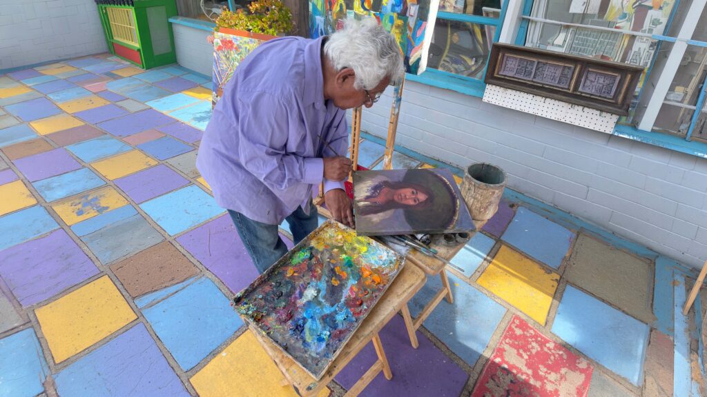 Edward Juarez painting on the colorful patio at Spanish Village Art Center